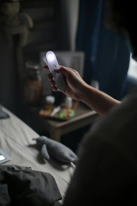 a person sitting on a bed holding a cell phone, holding up a night lamp, keylight, lumi, lit from behind