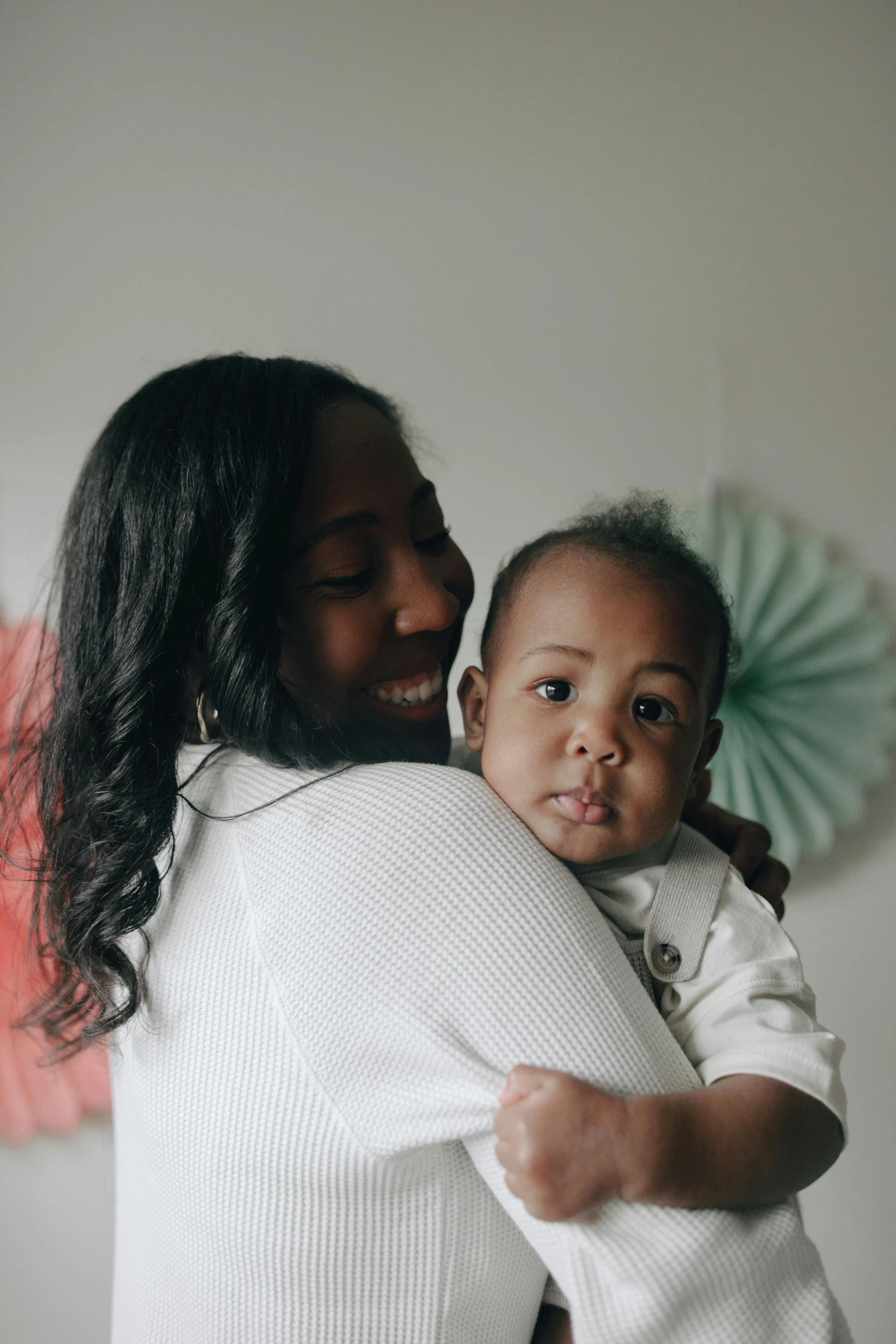 a woman holding a baby in her arms, by Lily Delissa Joseph, pexels contest winner, looking to the side off camera, black, carson ellis, proud looking