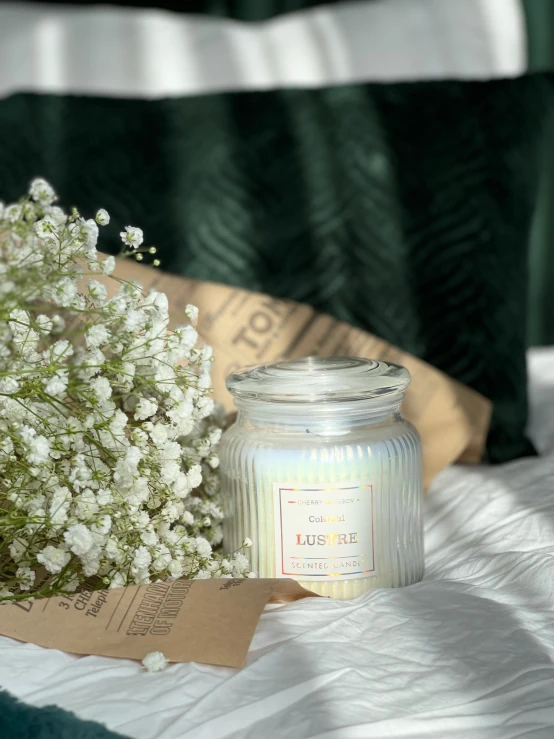 a glass jar sitting on top of a bed next to a bouquet of flowers, inspired by Lam Qua, light iridescent color, product image, in a room full of candles, alternate angle