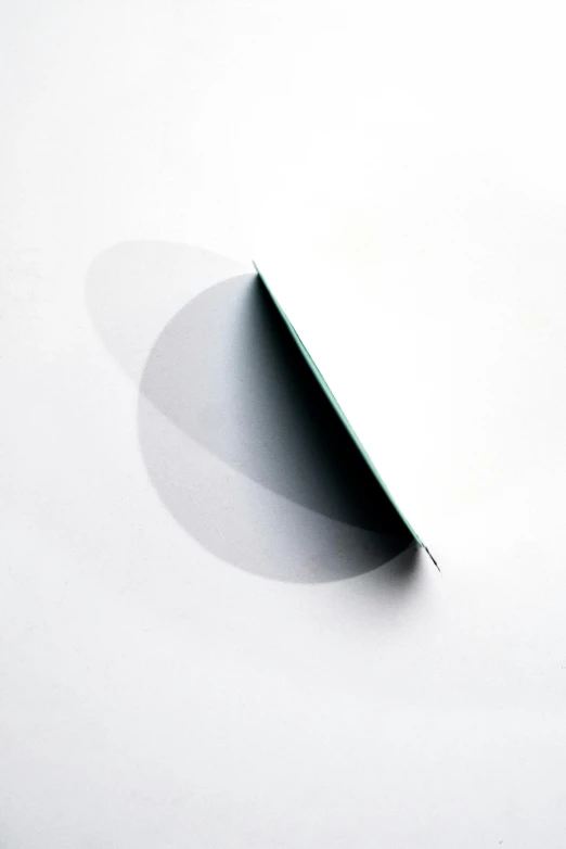 a piece of paper sitting on top of a table, inspired by Lucio Fontana, abstract illusionism, white background with shadows, half moon, teal gradient, wild angle lens