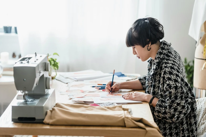 a woman sitting at a table in front of a sewing machine, a drawing, by Nicolette Macnamara, trending on pexels, japanese clothes, quality draughtmanship, wearing a designer top, cardboard