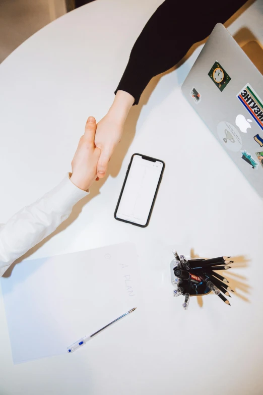 two people shaking hands in front of a laptop, by Sebastian Vrancx, pexels contest winner, taken on iphone 14 pro, white table, holding a staff, no - text no - logo