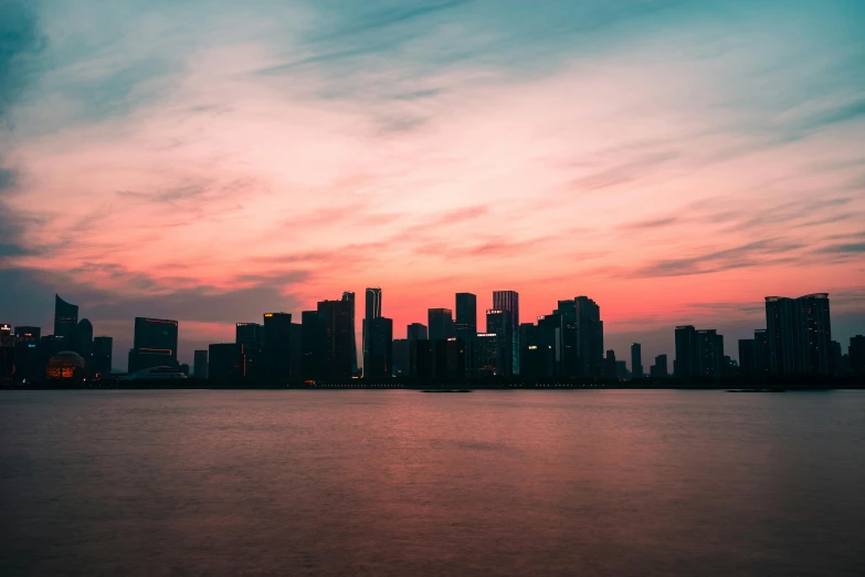 a large body of water with a city in the background, pexels contest winner, minimalism, redpink sunset, miami vice, skyline showing, binary sunset