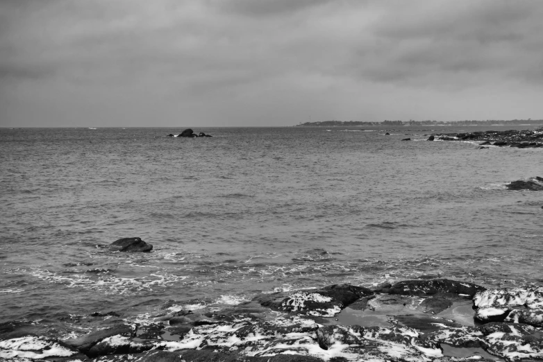 a black and white photo of the ocean, a black and white photo, by Thomas Fogarty, pexels, gloomy weather. high quality, black rocks, panorama, today\'s featured photograph 4k
