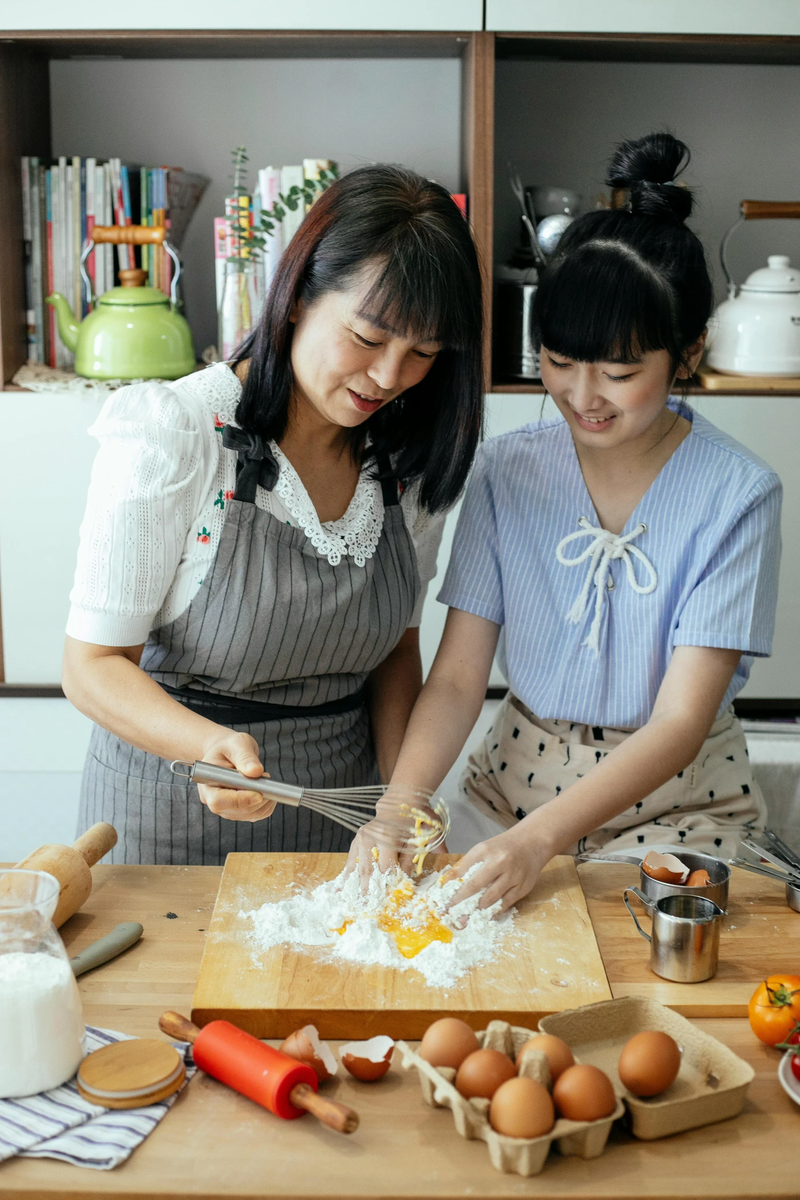 a couple of women standing next to each other in a kitchen, a portrait, inspired by Yukimasa Ida, pexels, baking cookies, promotional image, taiwan, chopping hands