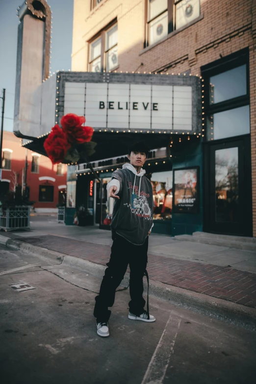 a man standing in front of a movie theater, an album cover, unsplash contest winner, realism, wearing a hoodie and flowers, downtown, he can ’ t believe his eyes, justin sun