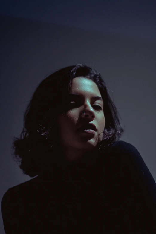 a black and white photo of a woman in a dark room, an album cover, inspired by Elsa Bleda, unsplash, aubrey plaza, mixed-race woman, deep colour, slightly overexposed