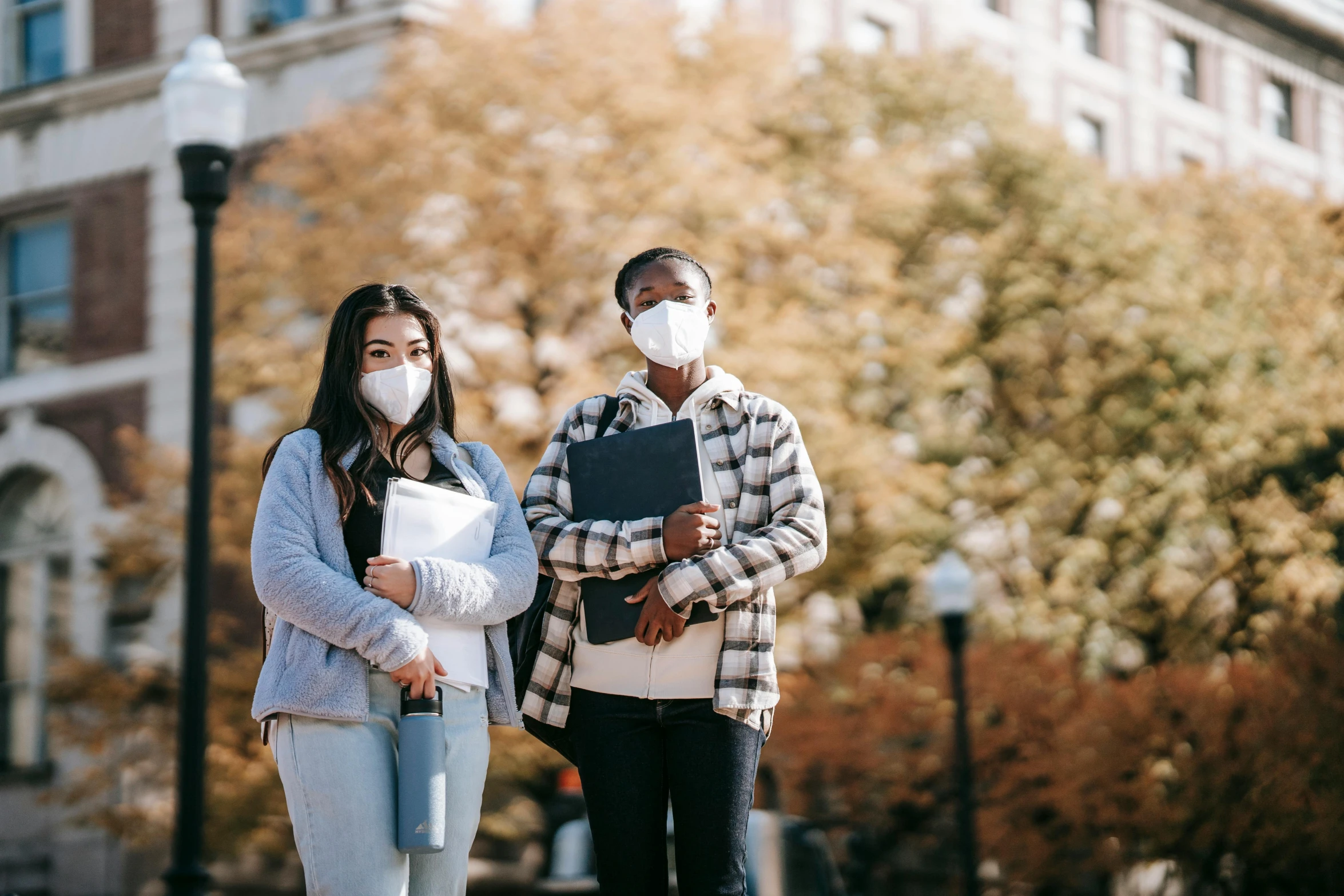 two people standing in front of a building wearing face masks, trending on pexels, renaissance, college girls, background image, diverse, wide-shot