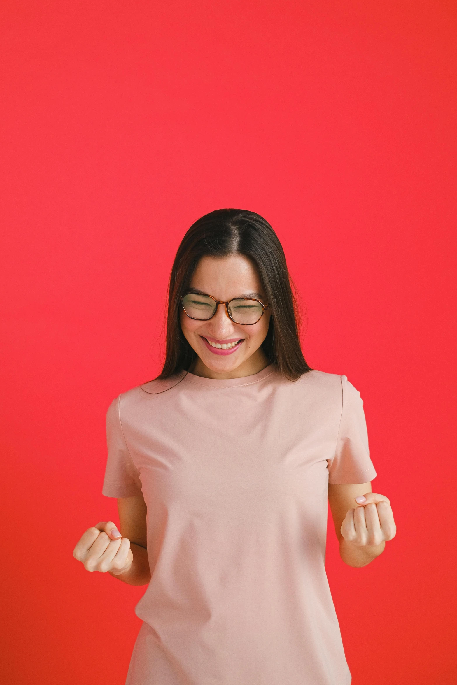 a woman standing in front of a red background, glasses |, excited, wearing casual clothing, optimistic