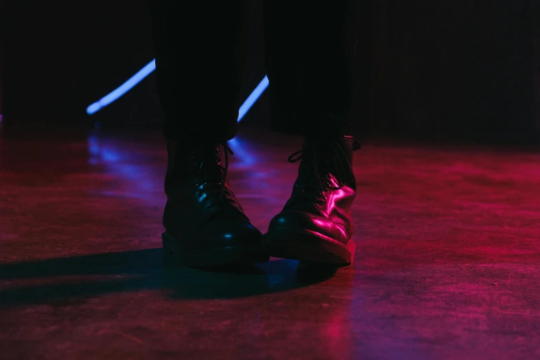 a person standing in front of a red light, an album cover, pexels contest winner, combat boots, reflecting light in a nightclub, purple and blue leather, empty stage