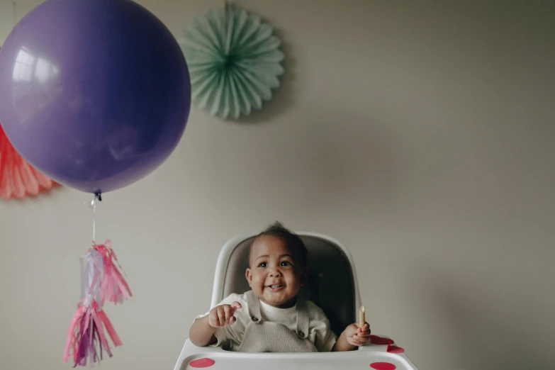 a baby sitting in a high chair in front of a balloon, pexels contest winner, purple themed, youthful taliyah, he is happy, cinematic wide shot