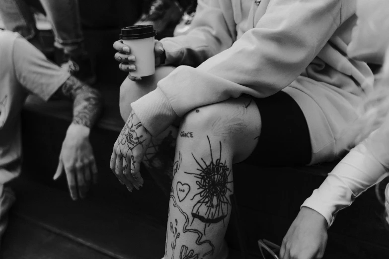 a black and white photo of a person with tattoos on their legs, a tattoo, by Emma Andijewska, pexels, graffiti, coffee cup, 🌸 🌼 💮, concert, stitches