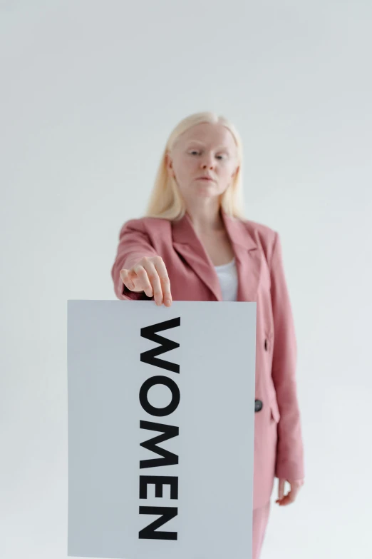 a woman holding a sign with the word women on it, an album cover, by Matija Jama, pexels contest winner, intense albino, business, computer, moma