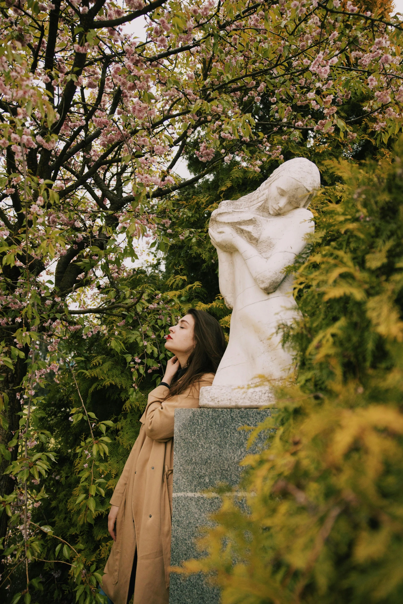 a woman standing next to a statue in a park, inspired by Elsa Bleda, unsplash, romanticism, blossoms, hooded, classical marble sculpture, instagram picture