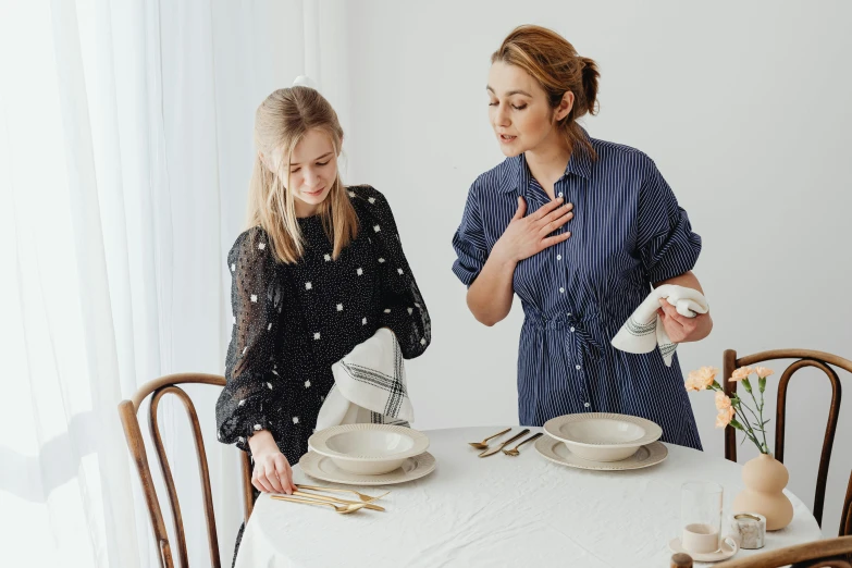 a woman standing next to a woman sitting at a table, by Alice Mason, pexels contest winner, wearing a linen shirt, serving body, polka dot, family friendly