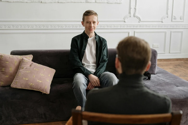 a man sitting on top of a couch next to a woman, a picture, pexels, young boy, séance, promotional image, school class