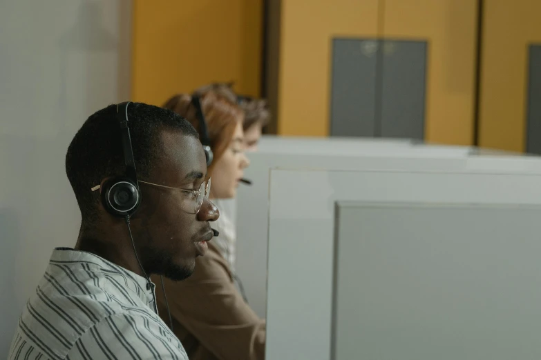 a man wearing a headset sitting in front of a computer, trending on pexels, hurufiyya, medium shot of two characters, group of people, ignant, varying ethnicities