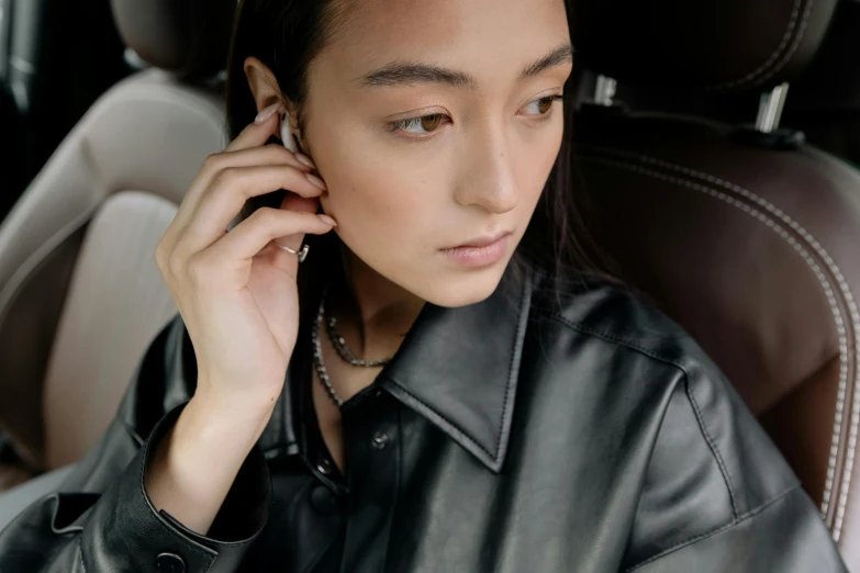 a woman sitting in a car talking on a cell phone, by Nina Hamnett, trending on pexels, happening, earbuds jewelry, portrait sophie mudd, wearing studded leather, promotional image