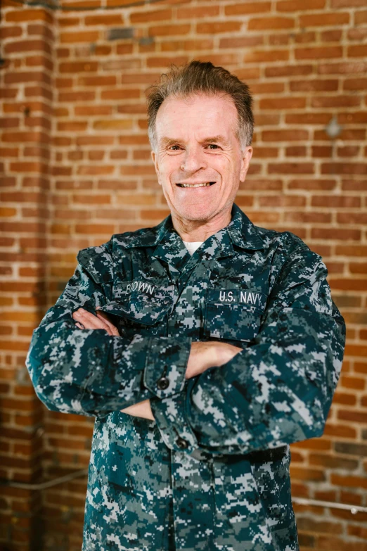 a man in uniform standing in front of a brick wall, naval background, adi meyers, lynn skordal, arms crossed