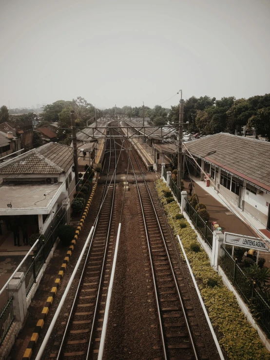 a train traveling down train tracks next to a train station, a picture, pexels contest winner, hyperrealism, indonesia, photo on iphone, wide high angle view, hazy and dreary