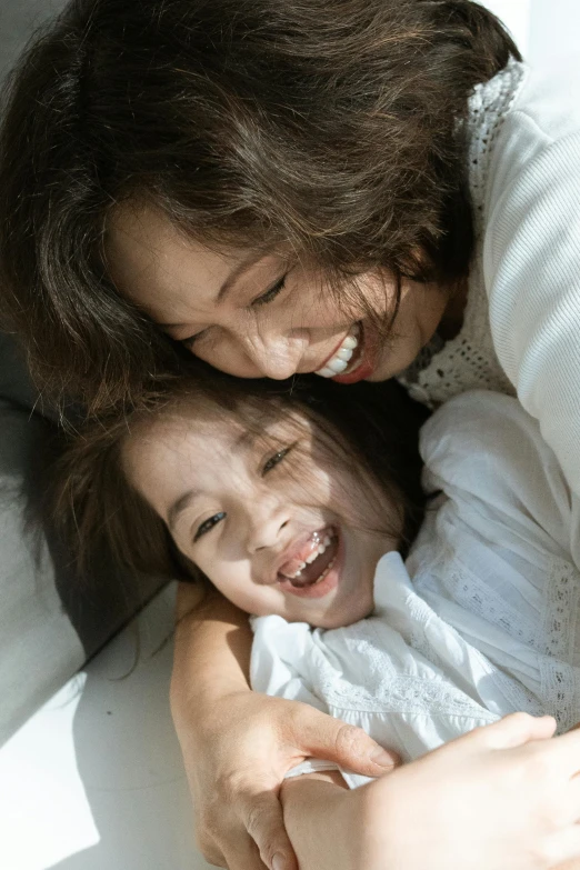 a woman holding a small child on top of a bed, pexels contest winner, smiling down from above, young asian girl, head bent back in laughter, slide show