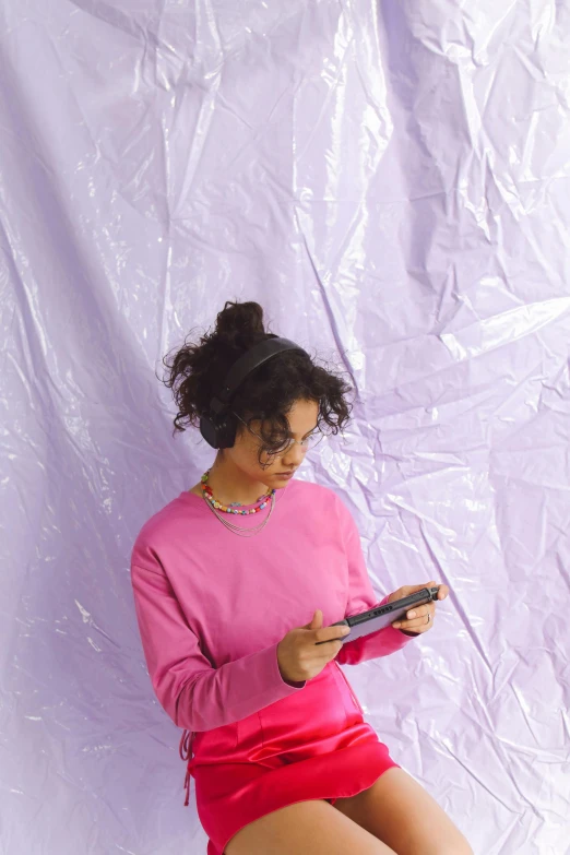 a woman sitting on a stool using a cell phone, an album cover, by Penelope Beaton, trending on pexels, video art, wearing a purple sweatsuit, pink volumetric studio lighting, holding a nintendo switch, imaan hammam