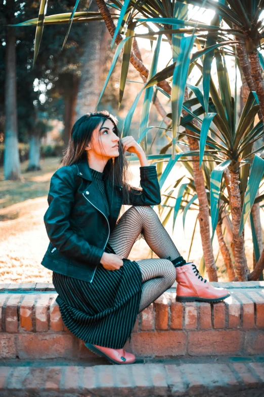 a woman sitting on top of a brick wall, by Julia Pishtar, pexels contest winner, dressed in short leather jacket, beautiful iranian woman, at a park, women full body