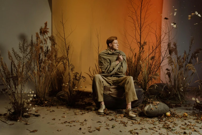 a man sitting in a chair in front of a wall, unsplash, magic realism, tilda swinton, spooky autumnal colours, eleanor tomlinson, sitting on a martian rock