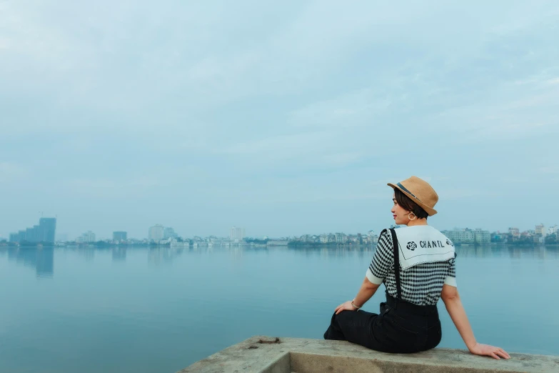 a woman sitting on a ledge overlooking a body of water, by Daniel Lieske, pexels contest winner, dang my linh, wearing stripe shirt, haze over the shoulder shot, an young urban explorer woman