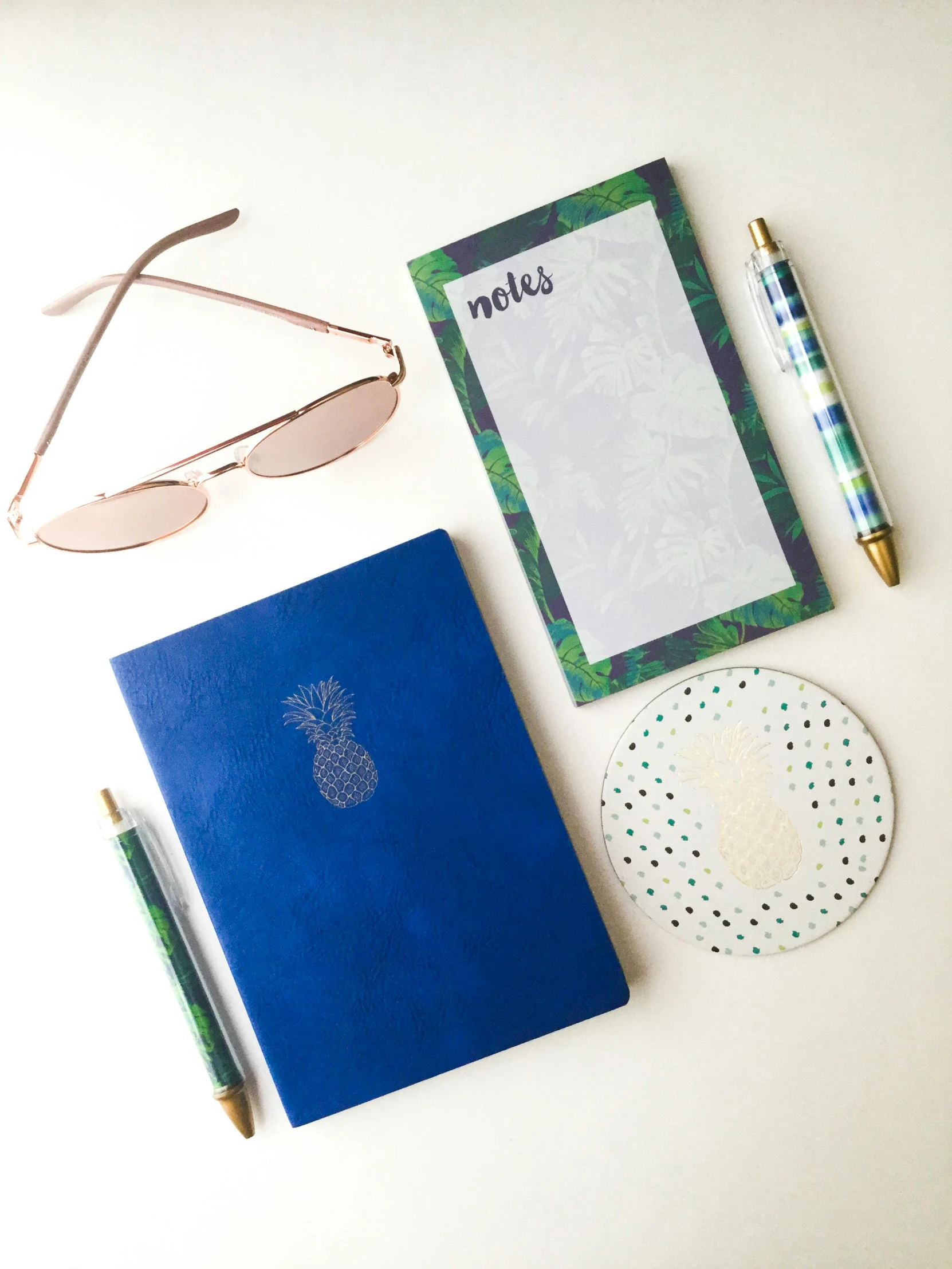 a notebook, pen, glasses, and a notepad on a table, by Rachel Reckitt, tropical style, gold and cobalt tiles, medium close shot, pineapple