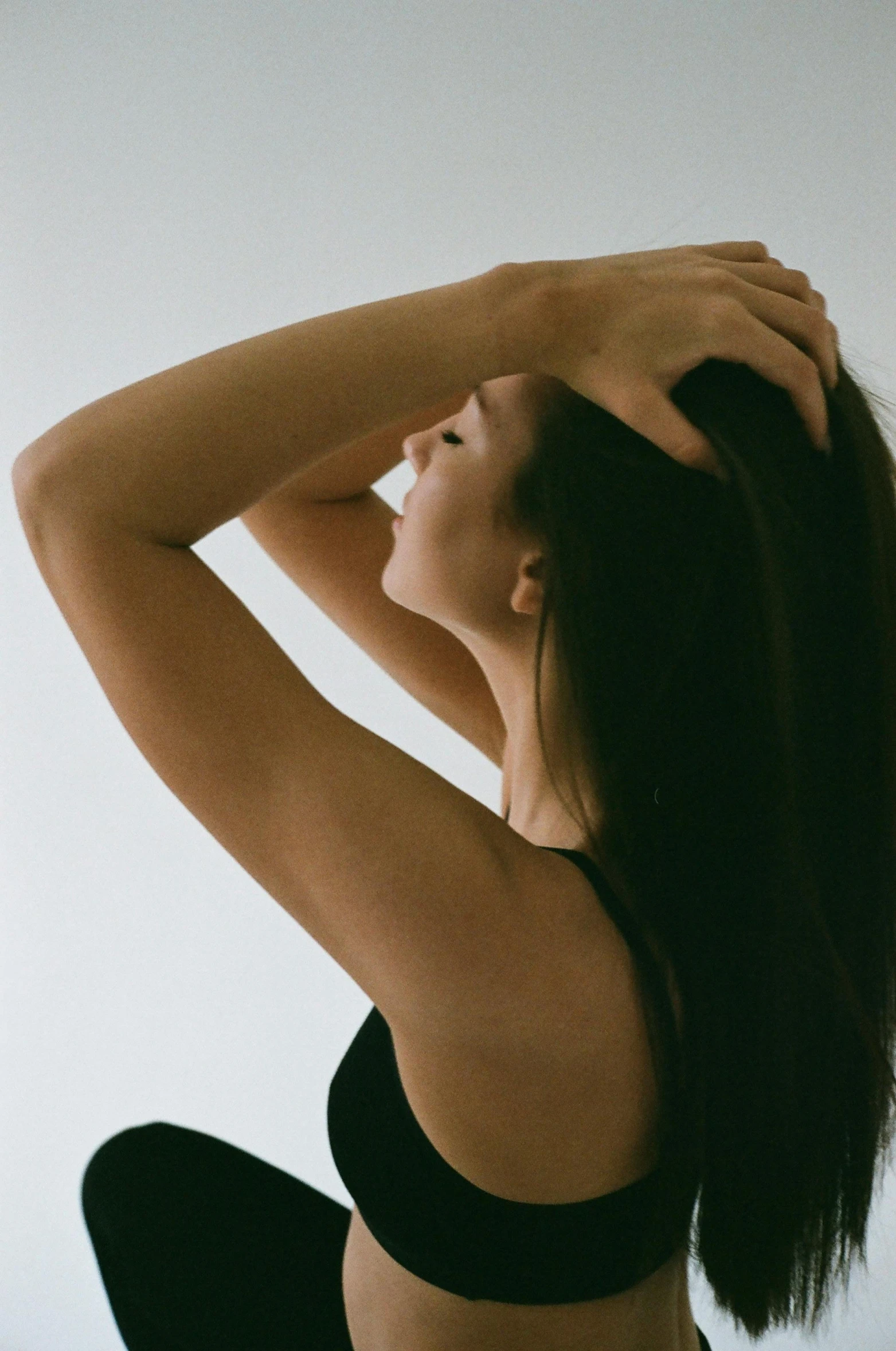 a woman in a black bra top doing a yoga pose, inspired by Ren Hang, unsplash, renaissance, hands in her hair. side-view, perfect silky straight hair, hair : long brown, long thin black hair