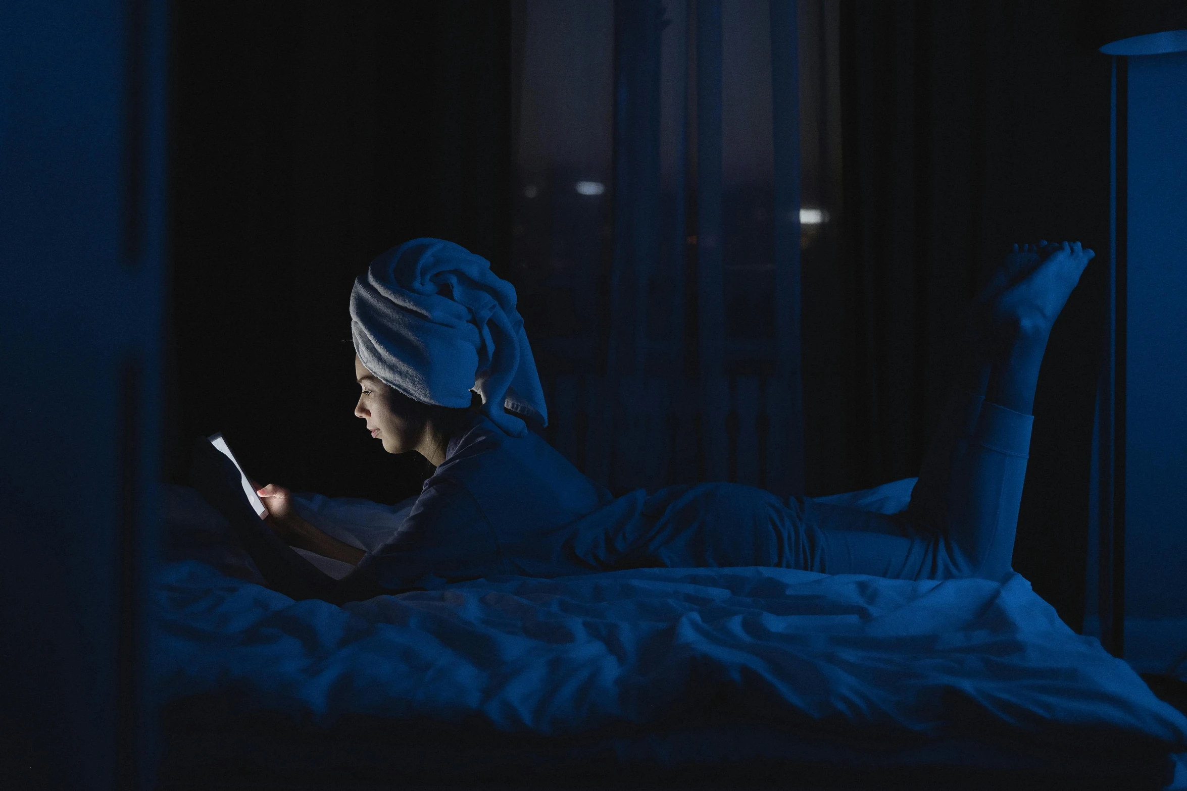 a woman laying in bed using a cell phone, inspired by Elsa Bleda, happening, long night cap, blue hue, reading, gaming