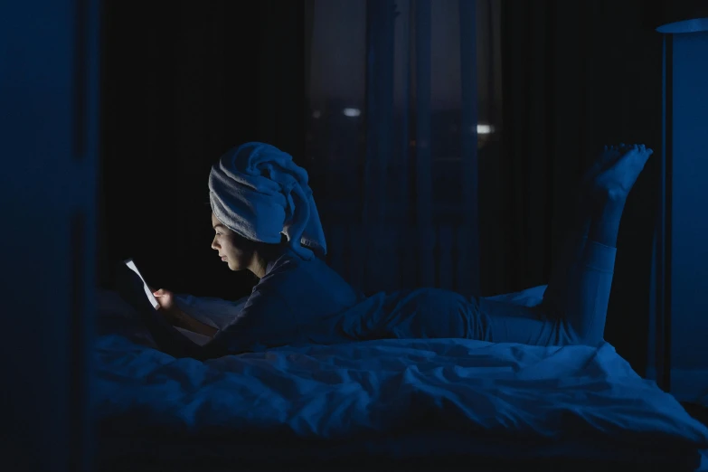 a woman laying in bed using a cell phone, inspired by Elsa Bleda, happening, long night cap, blue hue, reading, gaming