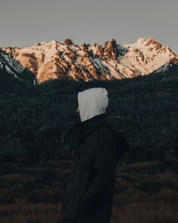 a person standing in front of a mountain, wearing a beanie, wearing pointed hoods, trending photo, no watermarks