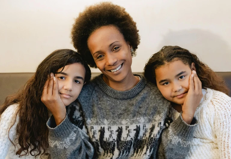 a woman sitting next to two girls on a couch, pexels contest winner, hurufiyya, mixed race woman, lovingly looking at camera, winter season, avatar image