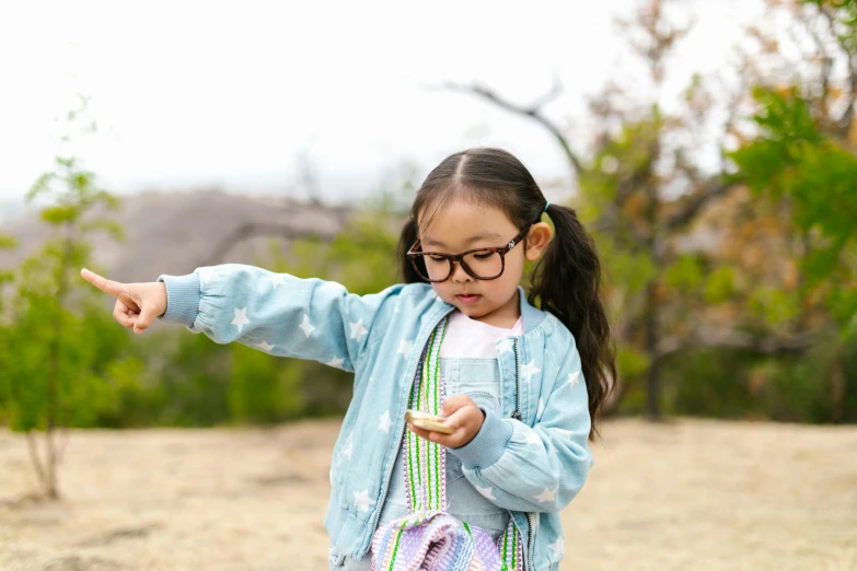 a little girl standing on top of a dirt field, a portrait, inspired by Hikari Shimoda, unsplash, square glasses, cardistry, checking her phone, glasses |