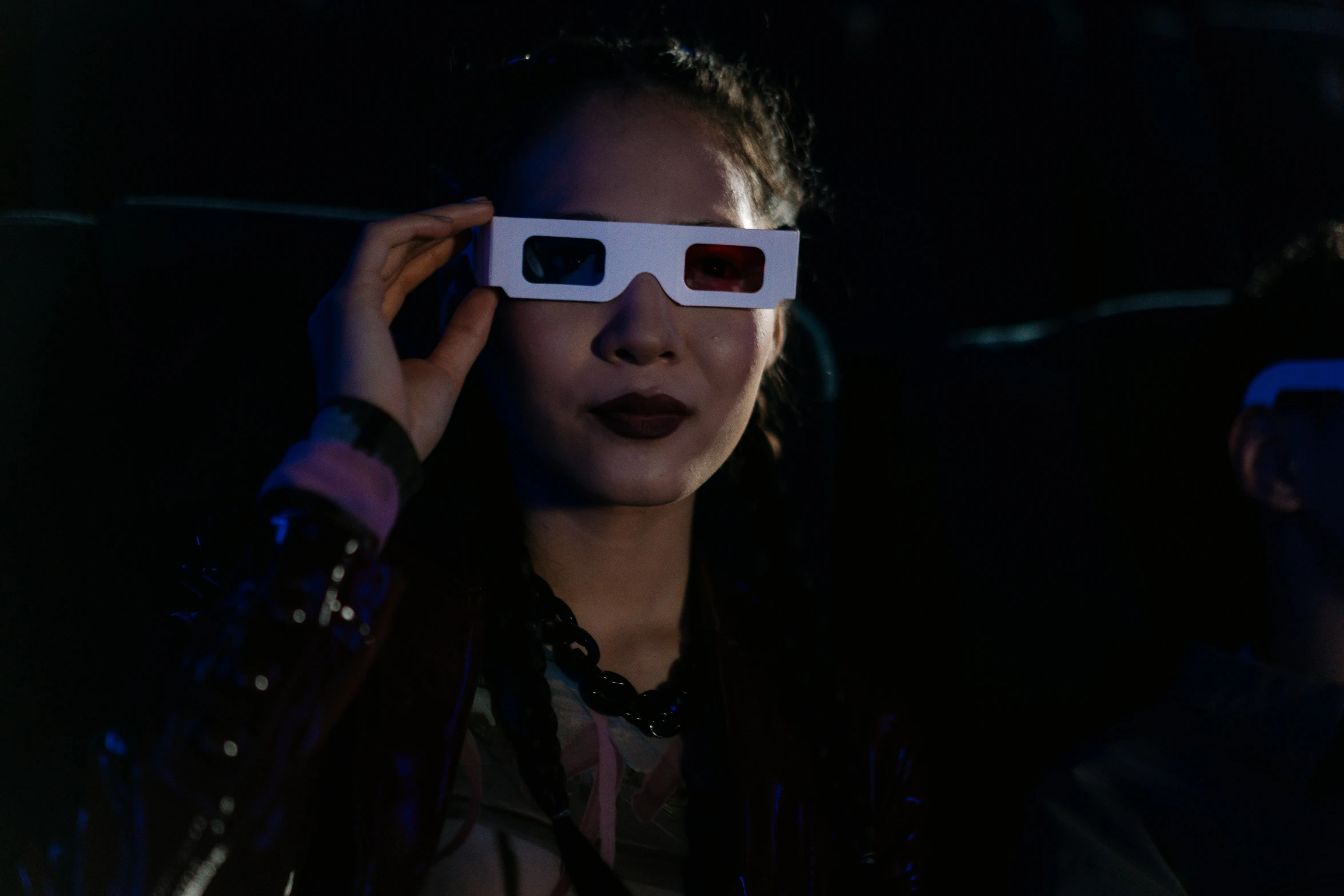 a woman holding a pair of glasses in front of her face, a hologram, inspired by Zhu Da, drive in movie theater, group of people in a dark room, wearing goggles, a young asian woman