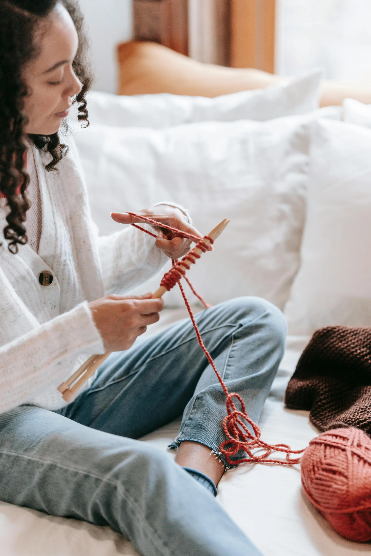 a woman sitting on a bed knitting a ball of yarn, trending on pexels, holding a wooden staff, wearing a red turtleneck sweater, promotional image, casual clothing