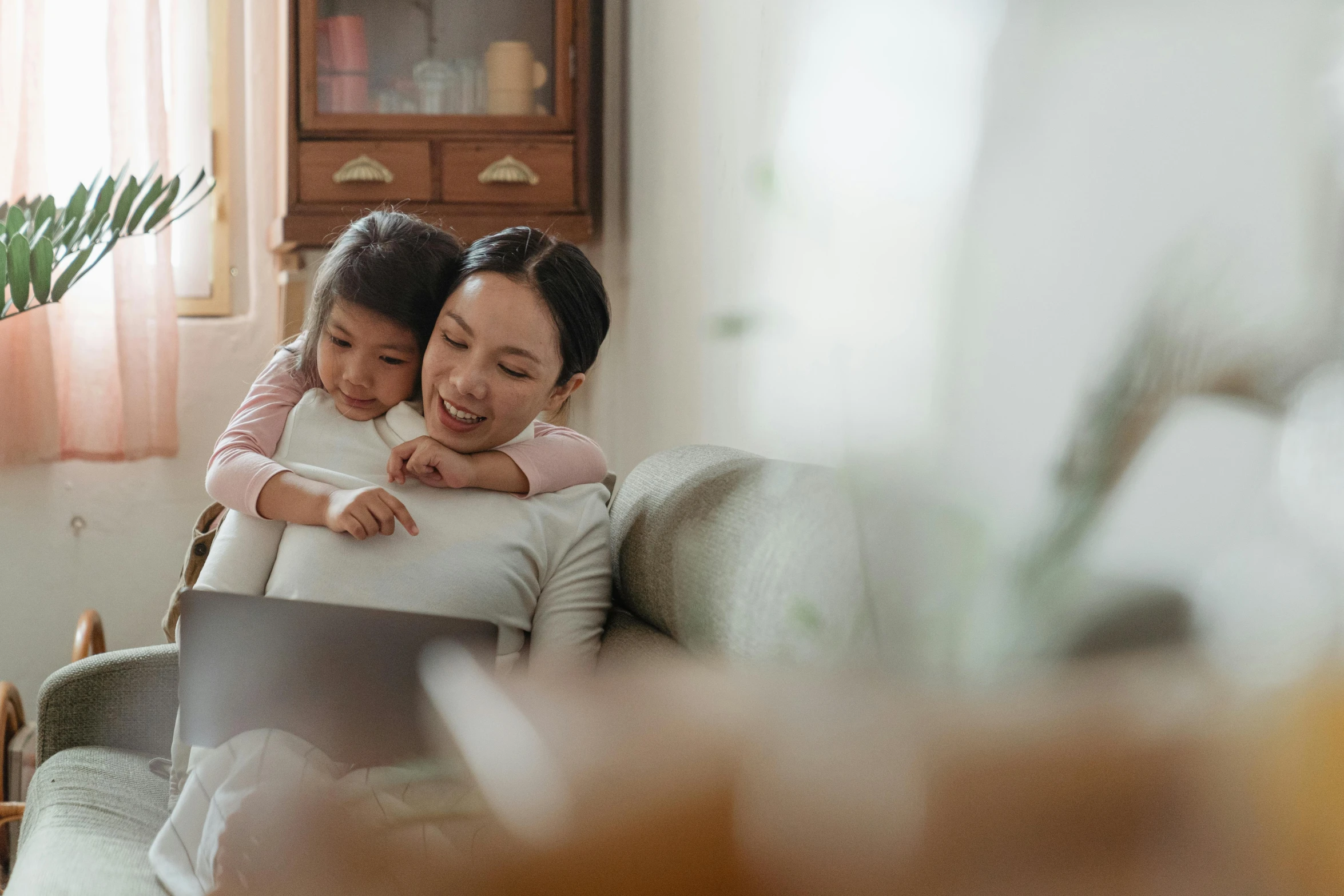 a woman and a child are sitting on a couch, pexels contest winner, computer art, young asian woman, everything fits on the screen, holding each other, marketing photo