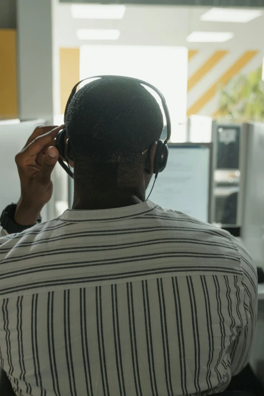 a man wearing headphones sitting in front of a computer, african canadian, facing away, in an call centre office, slightly pixelated