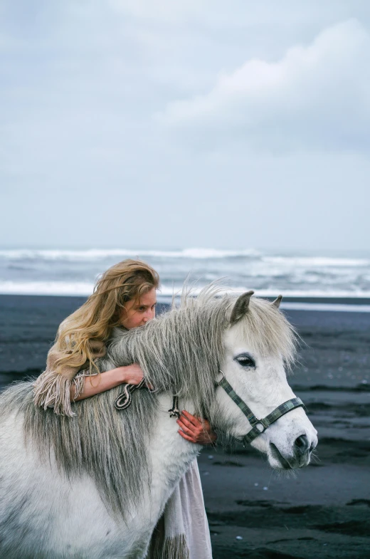 a woman standing next to a white horse on a beach, inspired by Annie Leibovitz, trending on unsplash, renaissance, iceland, square, bruce weber, black sand