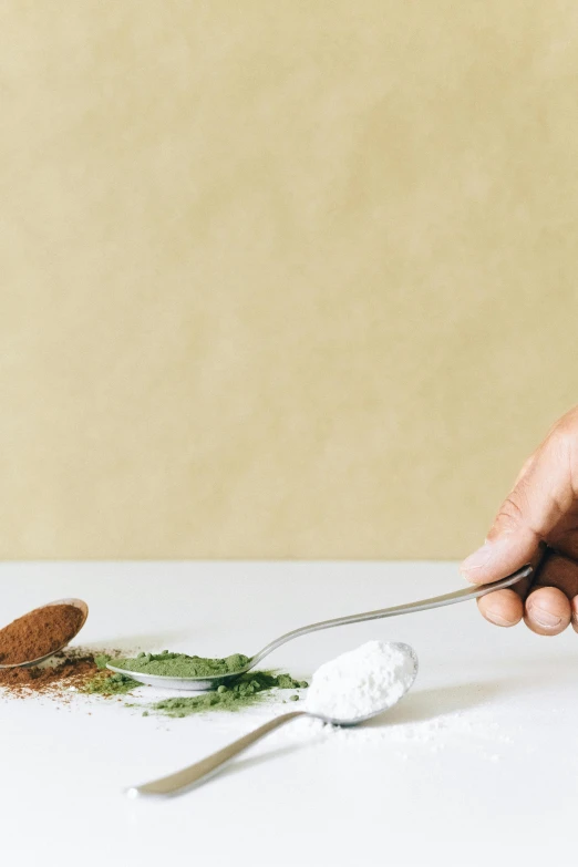 a person holding a spoon with some food on it, powder, tabletop, center of image, epicurious