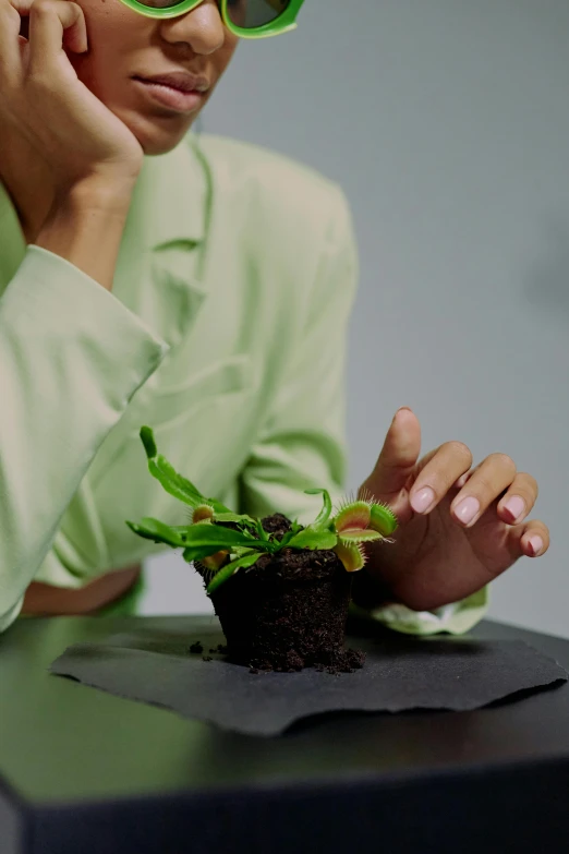 a woman sitting at a table with a plant in her hand, terraformation, bio-inspired design, nitrogen-rich soil, ignant