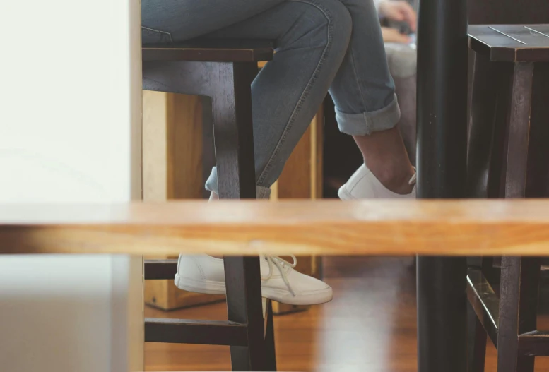 a woman sitting on top of a wooden table, trending on unsplash, white shoes, cafe interior, waiting to strike, people at work