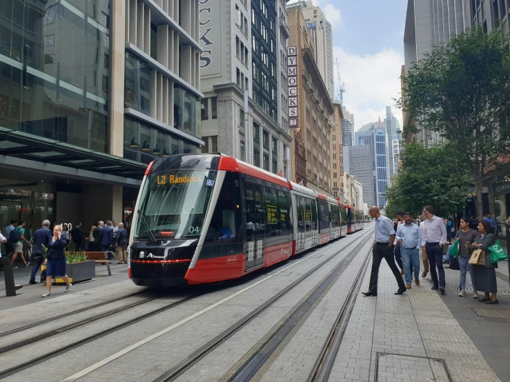 a red and black train traveling down a city street, hurufiyya, sydney, avatar image, heavily upvoted, people walking around