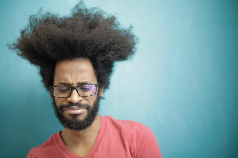 a man with a beard and glasses standing in front of a blue wall, an album cover, by Washington Allston, pexels, samurai with afro, stressed expression, close - up photograph, tinnitus