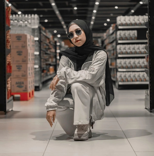 a woman sitting on the floor in a store, by Ismail Acar, pexels contest winner, she is wearing streetwear, shades of grey, confident stance, muslim