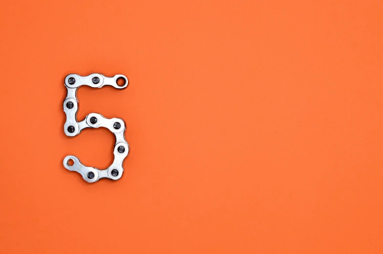 a close up of a bicycle chain on an orange background, trending on pexels, assemblage, five fingers, sacred numbers, metal font, 5 years old