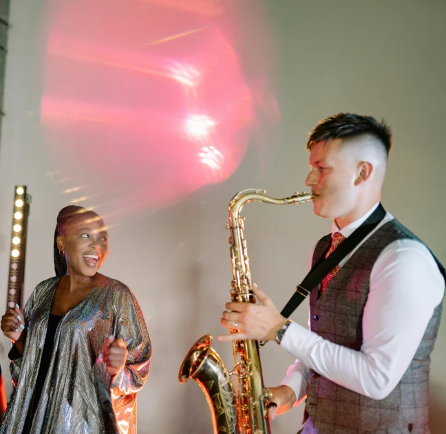 a man standing next to a woman playing a saxophone, bright lights, rhys lee, wedding, grace jones