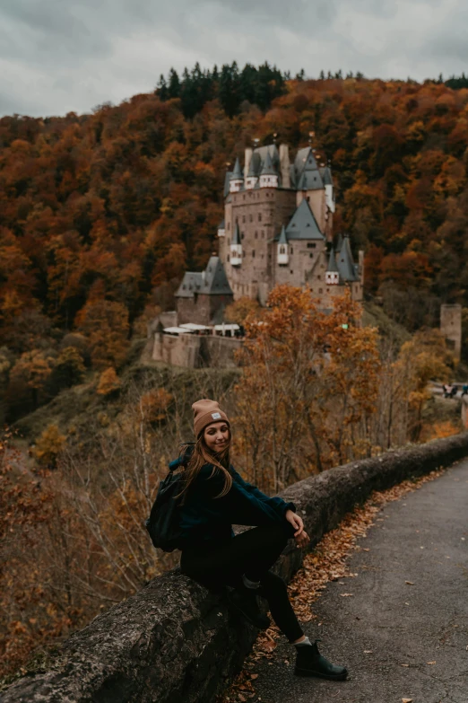 a woman sitting on a wall in front of a castle, by Johannes Voss, unsplash contest winner, 🍂 cute, german forest, 🎀 🧟 🍓 🧚, with trees